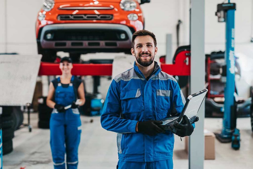 A person kneeling beside a car, closely inspecting the brake assembly with the wheel removed.