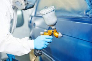 Person checking under a car hood with a visible battery and clean terminals in a suburban driveway.