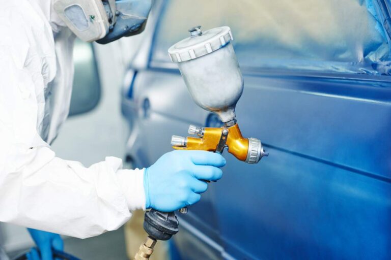 Person checking under a car hood with a visible battery and clean terminals in a suburban driveway.