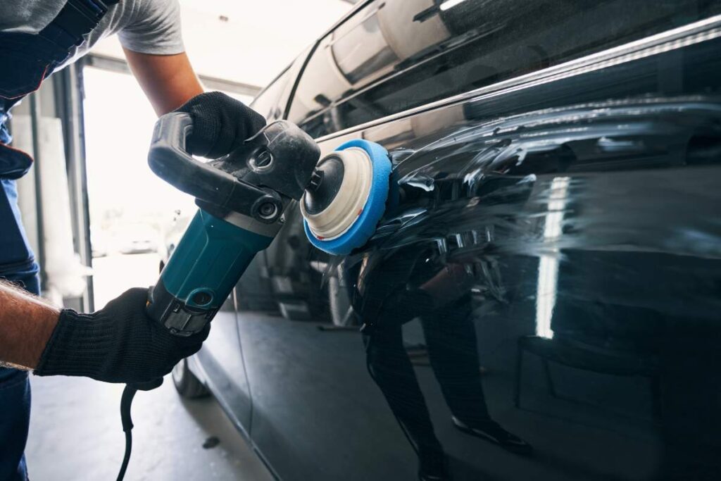 A person in casual clothing inspecting a car engine with the hood raised on a residential street.