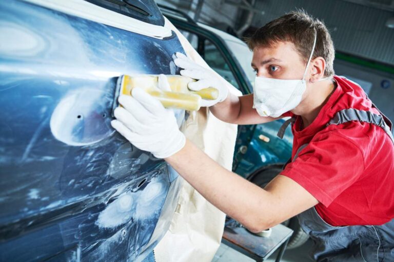 Technician measures wheel angles on a vehicle while inspecting tires and suspension components.